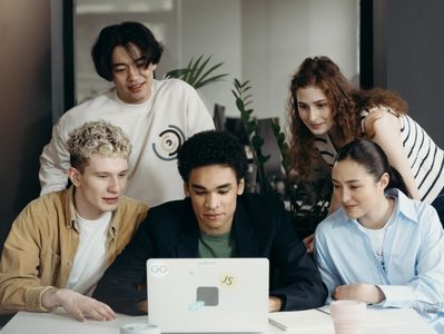 A group of people sitting around a table looking at a laptop.